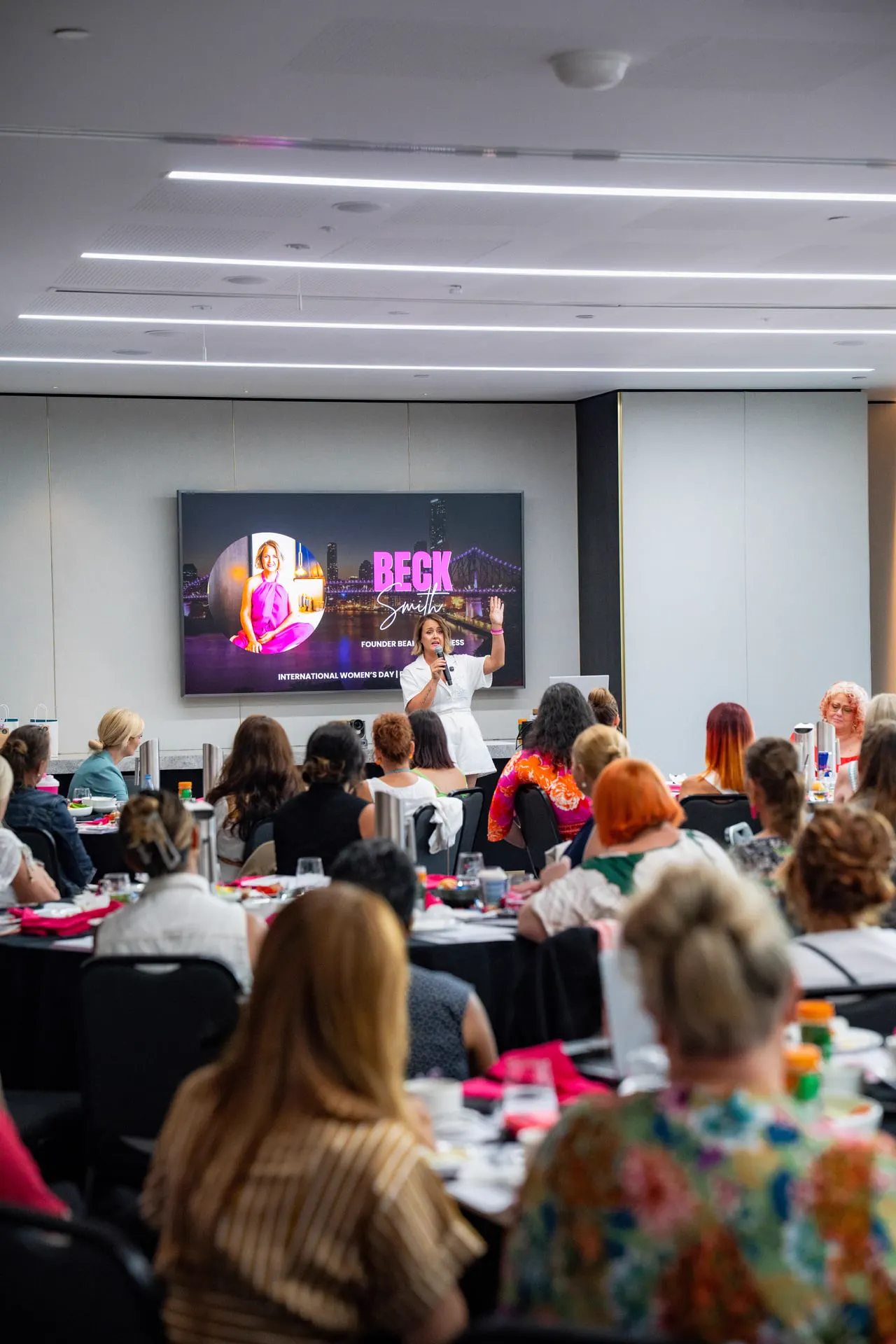 Beck Smith speaking on stage to a full conference room