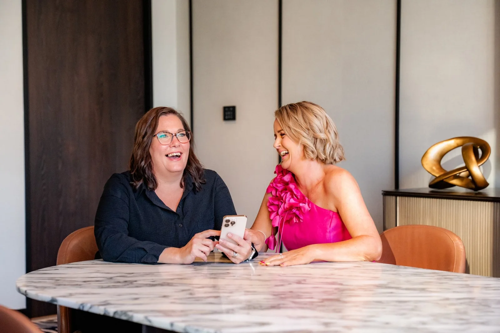 Two people sharing a conversation at a marble table, one wearing RAYE fuchsia.