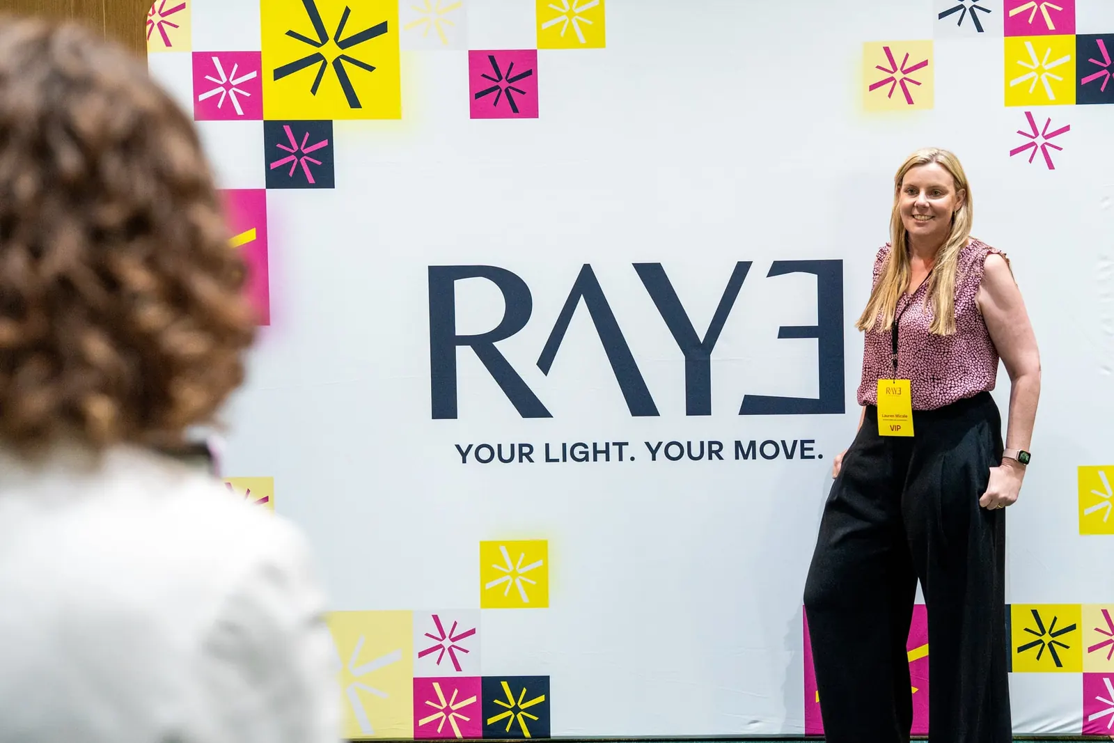 A RAYE Haus guest posing in front of the event wall