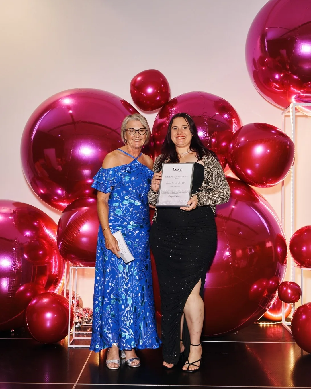 Two award recipients holding a Beam award certificate in front of red and pink balloons